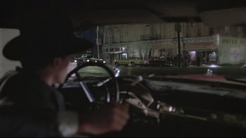 Movie still from “Wise Blood” (1979), directed by John Huston – A man driving a car at night in the dark; Wide shot, Over the shoulder angle