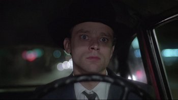 A man in a suit and hat driving a car