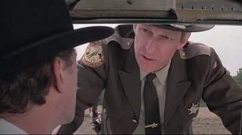Movie still from “Wise Blood” (1979), directed by John Huston – A man in a uniform talking to another man in a hat; Close Up shot, Over the shoulder angle