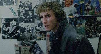 Movie still from “Withnail & I” (1987), directed by Bruce Robinson – A young man in front of a bunch of pictures; Close Up shot, Over the shoulder angle