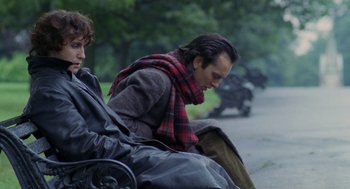 Movie still from “Withnail & I” (1987), directed by Bruce Robinson – A man sitting on top of a bench next to another man; Medium shot, Low angle