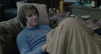 Movie still from “Withnail & I” (1987), directed by Bruce Robinson – A man is sitting in a chair and looking at a book; Medium shot, High angle