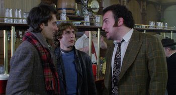 Movie still from “Withnail & I” (1987), directed by Bruce Robinson – A group of men standing next to each other in a room; Medium shot, Over the shoulder angle