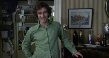 Movie still from “Withnail & I” (1987), directed by Bruce Robinson – A man in a green shirt standing next to a wine bottle; Medium shot, Over the shoulder angle