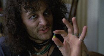 Movie still from “Withnail & I” (1987), directed by Bruce Robinson – A man holding a pill bottle in front of his face; Close Up shot, Over the shoulder angle