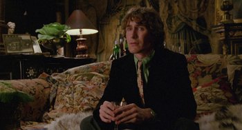 Movie still from “Withnail & I” (1987), directed by Bruce Robinson – A man sitting on top of a couch holding a wine glass; Medium shot, Low angle