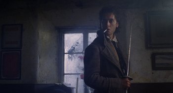 Movie still from “Withnail & I” (1987), directed by Bruce Robinson – A man holding a sword in a room with a window; Medium shot, Low angle