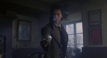 Movie still from “Withnail & I” (1987), directed by Bruce Robinson – A man in a suit and tie holding a sword; Medium shot, Low angle