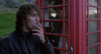 Movie still from “Withnail & I” (1987), directed by Bruce Robinson – A man smoking a cigarette while looking out of a phone booth; Close Up shot, Low angle