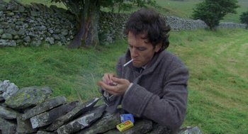 Movie still from “Withnail & I” (1987), directed by Bruce Robinson – A man sitting on top of a wooden bench smoking a cigarette; Close Up shot, High angle
