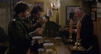 Movie still from “Withnail & I” (1987), directed by Bruce Robinson – A group of people sitting at a table with candles; Medium shot, Over the shoulder angle