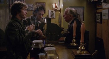 Movie still from “Withnail & I” (1987), directed by Bruce Robinson – A group of people sitting at a table with food; Medium shot, Over the shoulder angle