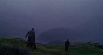 Movie still from “Withnail & I” (1987), directed by Bruce Robinson – Two people walking on a grassy hill near a body of water; Extreme Wide shot, High angle