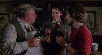 Movie still from “Withnail & I” (1987), directed by Bruce Robinson – A group of men standing around each other holding wine glasses; Medium shot, Over the shoulder angle