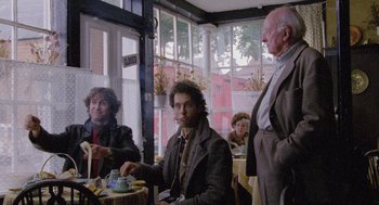 Movie still from “Withnail & I” (1987), directed by Bruce Robinson – A group of people sitting around a table; Medium shot, Low angle