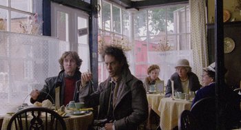Movie still from “Withnail & I” (1987), directed by Bruce Robinson – A group of people sitting at tables in a restaurant; Medium shot, Low angle