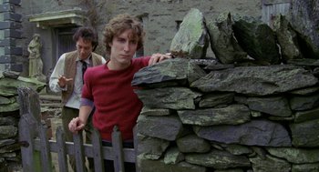 Movie still from “Withnail & I” (1987), directed by Bruce Robinson – A man leaning against a stone wall next to a fence; Medium shot, Low angle