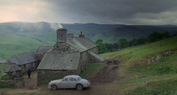 Movie still from “Withnail & I” (1987), directed by Bruce Robinson – An old car parked in front of an old stone house; Extreme Wide shot, High angle