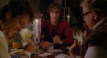 Movie still from “Withnail & I” (1987), directed by Bruce Robinson – A man sitting at a table playing cards with other people; Medium shot, Over the shoulder angle