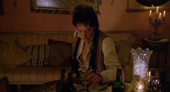 Movie still from “Withnail & I” (1987), directed by Bruce Robinson – A man sitting at a table with a glass of wine; Medium shot, Low angle