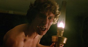 Movie still from “Withnail & I” (1987), directed by Bruce Robinson – A shirtless man holding a lit oil lamp in a dark room; Close Up shot, Low angle