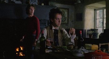 Movie still from “Withnail & I” (1987), directed by Bruce Robinson – A man sitting at a table with a wine glass; Medium shot, Low angle