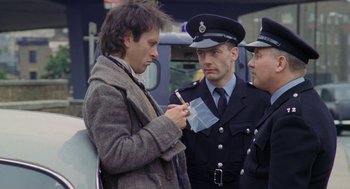 Movie still from “Withnail & I” (1987), directed by Bruce Robinson – Two police officers and a man looking at a piece of paper; Medium shot, Over the shoulder angle