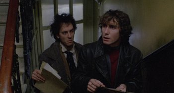 Movie still from “Withnail & I” (1987), directed by Bruce Robinson – Two men are standing next to each other holding papers; Medium shot, Over the shoulder angle