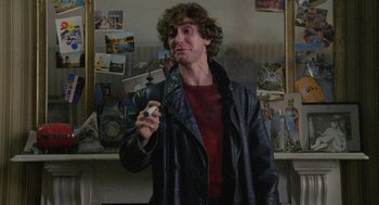Movie still from “Withnail & I” (1987), directed by Bruce Robinson – A man in a leather jacket holding a cell phone; Medium shot, Low angle