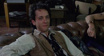 Movie still from “Withnail & I” (1987), directed by Bruce Robinson – A man sitting on top of a couch wearing a tie; Close Up shot, Over the shoulder angle