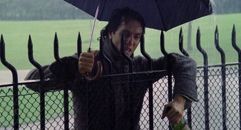 Movie still from “Withnail & I” (1987), directed by Bruce Robinson – A person holding an umbrella over a fence; Medium shot, Low angle
