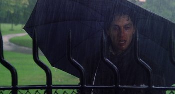 Movie still from “Withnail & I” (1987), directed by Bruce Robinson – A man holding an umbrella over his head while standing in the rain; Close Up shot, Low angle