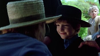 Movie still from “Witness” (1985), directed by Peter Weir – A young boy wearing a straw hat and a suit; Close Up shot, Over the shoulder angle