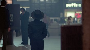 Movie still from “Witness” (1985), directed by Peter Weir – A person wearing a hat standing in a room; Wide shot, Over the shoulder angle