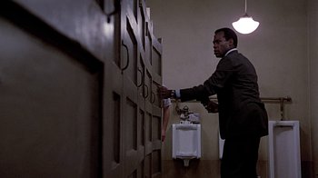 Movie still from “Witness” (1985), directed by Peter Weir – A man in a suit and tie touching a wall; Medium shot, Low angle