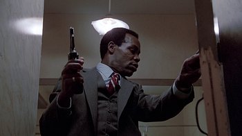 Movie still from “Witness” (1985), directed by Peter Weir – A man in a suit and tie holding a gun; Medium shot, Low angle
