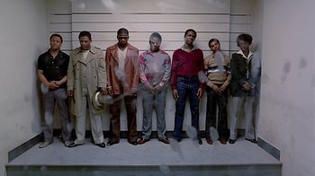 Movie still from “Witness” (1985), directed by Peter Weir – A group of men standing next to each other in front of a wall; Wide shot, Low angle