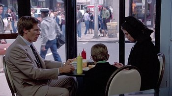 Movie still from “Witness” (1985), directed by Peter Weir – A group of people sitting at a table with food on it; Medium shot, Over the shoulder angle
