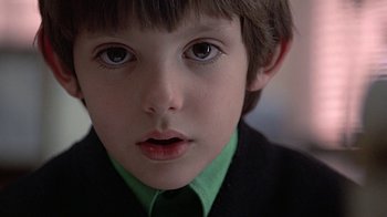 Movie still from “Witness” (1985), directed by Peter Weir – A young boy wearing a suit and tie; Close Up shot, Low angle
