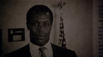 Movie still from “Witness” (1985), directed by Peter Weir – A man wearing a suit and tie in front of an american flag; Close Up shot, Low angle