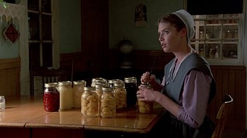 Movie still from “Witness” (1985), directed by Peter Weir – A woman in an old - fashioned dress is holding a jar of pickles; Medium shot, Over the shoulder angle