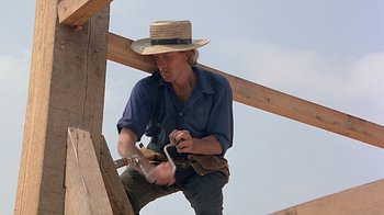 Movie still from “Witness” (1985), directed by Peter Weir – A man wearing a straw hat is using a saw to cut wood; Medium shot, Low angle