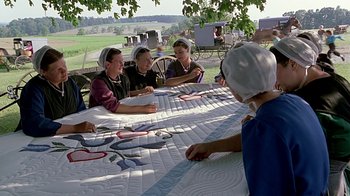Movie still from “Witness” (1985), directed by Peter Weir – A group of people sitting at a table with quilts on top of it; Wide shot, High angle