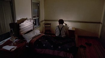 Movie still from “Witness” (1985), directed by Peter Weir – A person sitting on a bed looking at a book; Wide shot, High angle