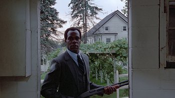 Movie still from “Witness” (1985), directed by Peter Weir – A man in a suit and tie holding a rifle; Medium shot, Low angle