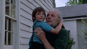 Movie still from “Witness” (1985), directed by Peter Weir – An older man holding a young boy in his arms; Close Up shot, Low angle