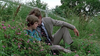 Movie still from “Witness” (1985), directed by Peter Weir – A man and a boy sitting in the grass; Medium shot, Low angle