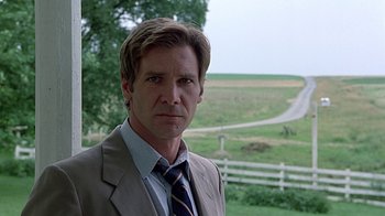 Movie still from “Witness” (1985), directed by Peter Weir – A man wearing a suit and tie standing in front of a field; Close Up shot, Over the shoulder angle