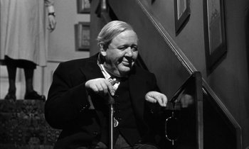 Movie still from “Witness for the Prosecution” (1957), directed by Billy Wilder – An older man sitting on a chair in a room; Medium shot, High angle