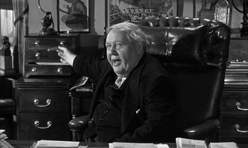 Movie still from “Witness for the Prosecution” (1957), directed by Billy Wilder – An older man sitting in a chair in a room; Medium shot, Over the shoulder angle